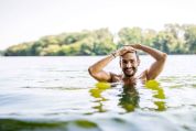 Mann mit gestutztem Vollbart guckt mit dem Kopf aus einem Natursee und streicht sich über seine Haare Mann mit gestutztem Vollbart guckt mit dem Kopf aus einem Natursee und streicht sich über seine Haare